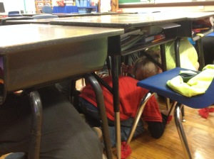 Student go through an earthquake drill by going underneath their desk and waiting for about 60 seconds.