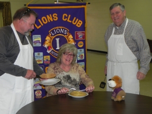 Clay Tarter (L) and Richard Ireton  (r)  prepare to serve a sampling of pancakes to Cheryl Tarter in preparation for the “Pancake Feast” held Friday, March 27th at the American Legion Building for both lunch and supper